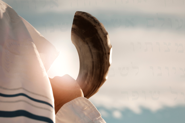 a person with a tallit over their head holds a shofar to their mouth