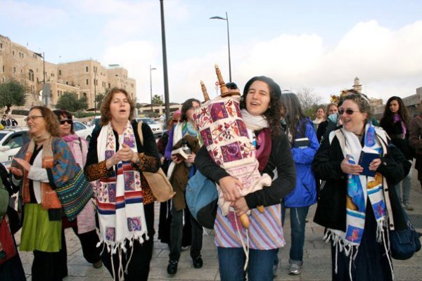 A group of women joyfully carrying a Torah scroll outdoors, wearing colorful scarves and prayer shawls.