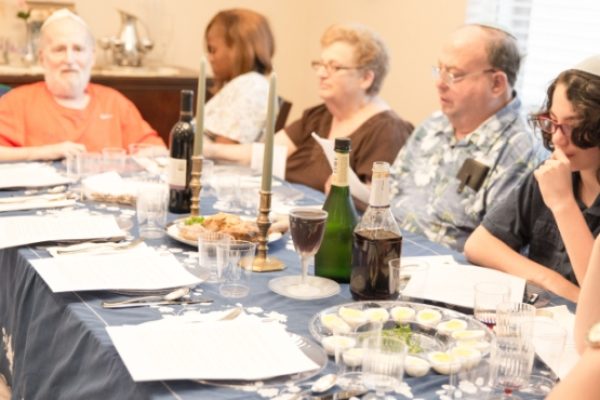 A family gathered around a table set with wine, candles, and food, engaged in conversation.