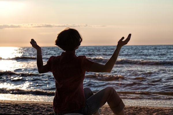 a person sits at the water's edge, lifting their hands upward