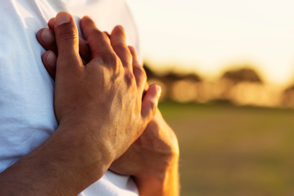 close up of person's hands on their chest outdoors in sunlight