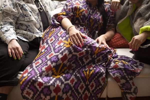 Three people with colorful clothing and nails sitting on a sofa, with focus on the patterned dress in the center.
