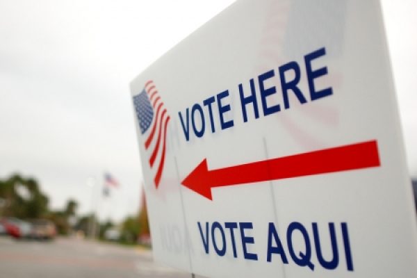Sign with an American flag graphic that reads VOTE HERE and VOTE AQUÍ with an arrow pointing right.