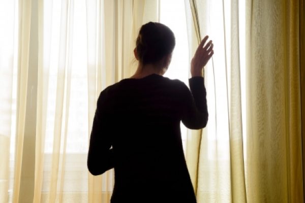 Silhouette of a person partially opening a sheer curtain, with soft natural light filling the room.