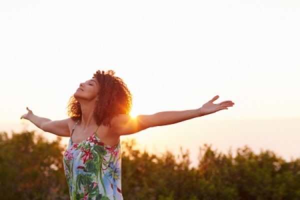 Woman with arms outstretched, enjoying sunset in nature, wearing a floral dress.