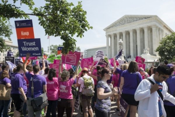 A diverse crowd gathers with colorful signs outside a large neoclassical building, advocating for womens rights.