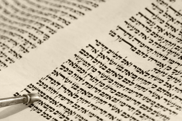 Close-up of a Torah scroll with Hebrew text and a yad (pointer) following the lines.