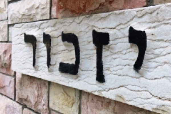 sign in hebrew that reads "yizkor" memorial - black letters on white stone