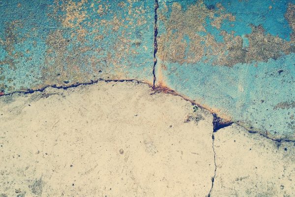a close=up of cracks in a wall, the surface is blue in places and beige below