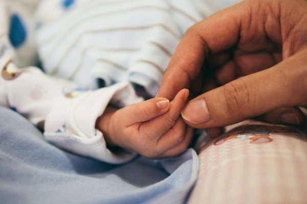 Adult hand gently holding a babys hand, both resting on a soft, patterned blanket.