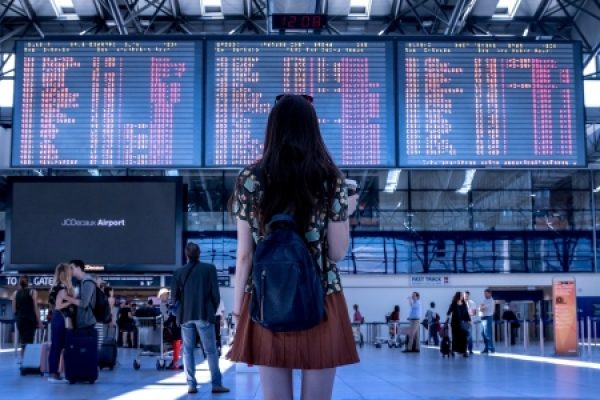 Woman with backpack looking at flight information board in an airport terminal.