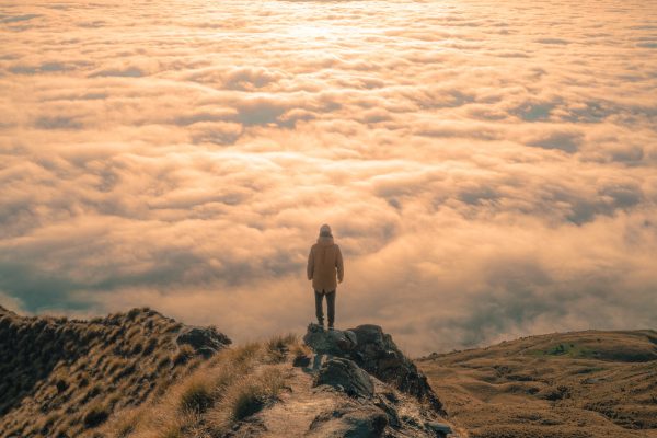 person standing on mountain in front of sea of clouds and sunshine