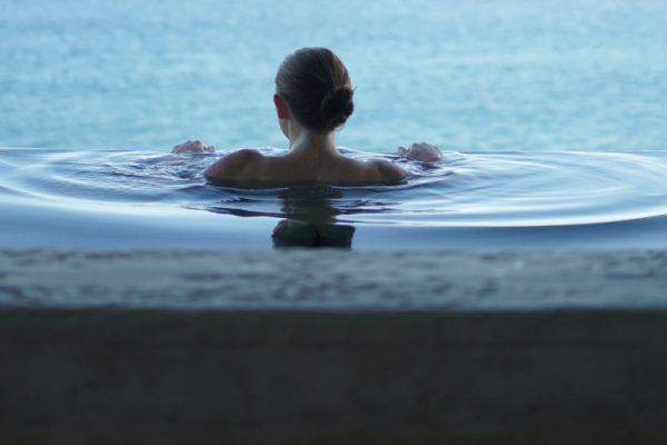 Person in an infinity pool, gazing out at the serene ocean view under a clear sky.
