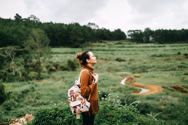 a woman stands alone walking into a grassy meadow