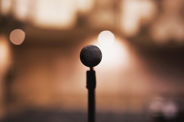 A close-up of a microphone on a stand with a blurred background and warm lighting.