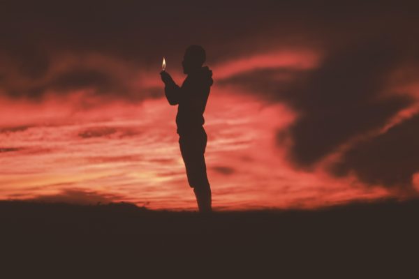 silhouette of a person holding a candle against a sunset