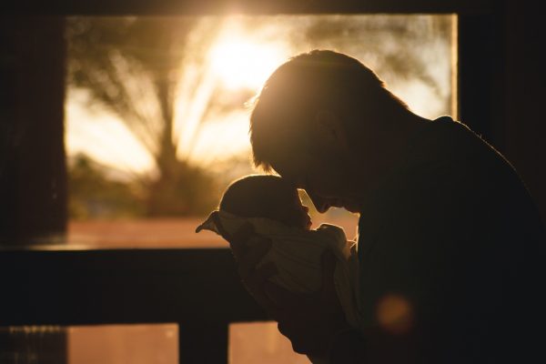Silhouette of a person holding a baby against a sunset backdrop by a window.