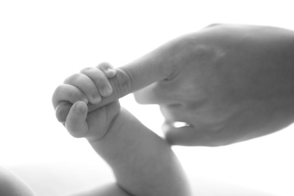 Close-up of a baby holding an adults finger, conveying a sense of connection and tenderness.