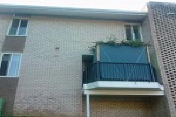 A two-story brick building with a small balcony and green-covered wall section.