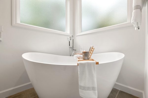 Minimalist bathroom with a white freestanding bathtub, wooden caddy, towels, and large frosted windows.