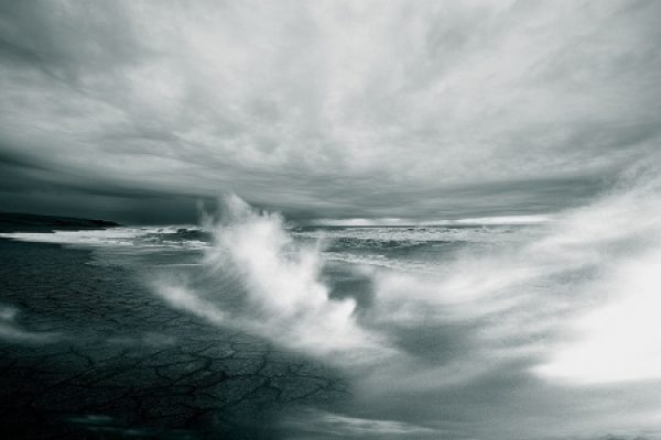 Monochrome image of a stormy sea with crashing waves and dark, cloudy skies.
