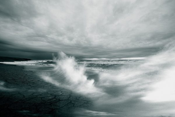 Dramatic seascape with crashing waves under a stormy, cloudy sky.