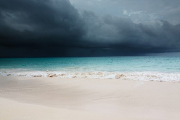 Stormy clouds gather over a calm beach with turquoise water and white sand.