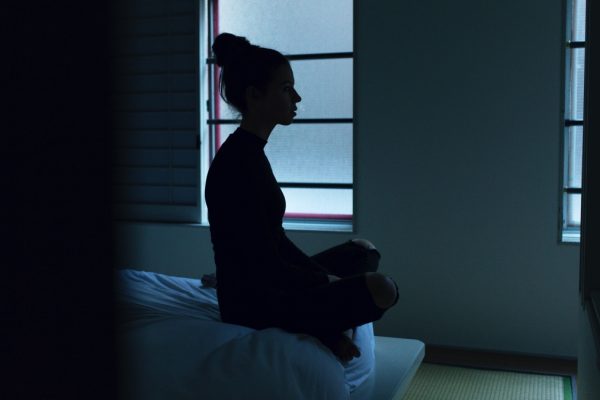 Silhouette of a person sitting in a dimly lit room, facing a window with soft, natural light coming in.
