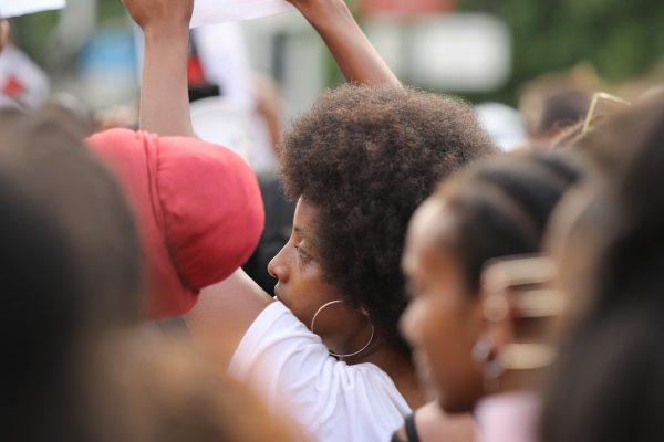 Person with afro hairstyle holding a sign at a crowded outdoor event, surrounded by others.