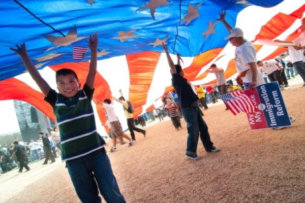 Children hold a large American flag at a rally; a sign reads My Voice, My Vote, Immigration Reform.