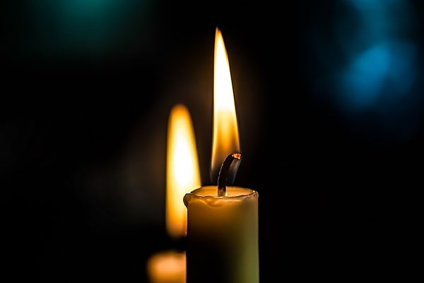 Close-up of two lit candles with glowing flames in a dark setting.