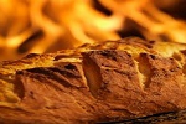 Golden loaf of bread baking in front of a glowing oven fire.