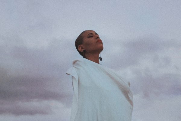 A person in a white outfit gazes upward against a cloudy sky.