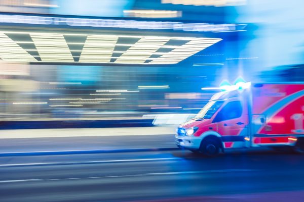 A red and white ambulance speeds down a city street with lights flashing at night.