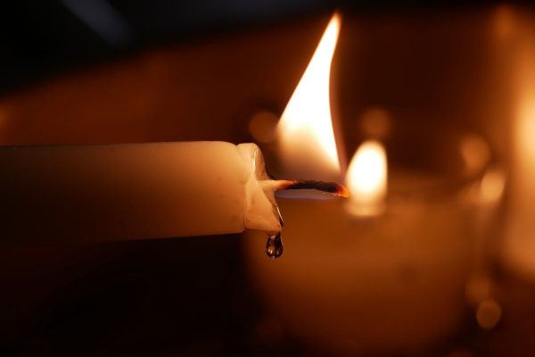 Close-up of a lit candle with a melting wax drip and soft flame in the background.