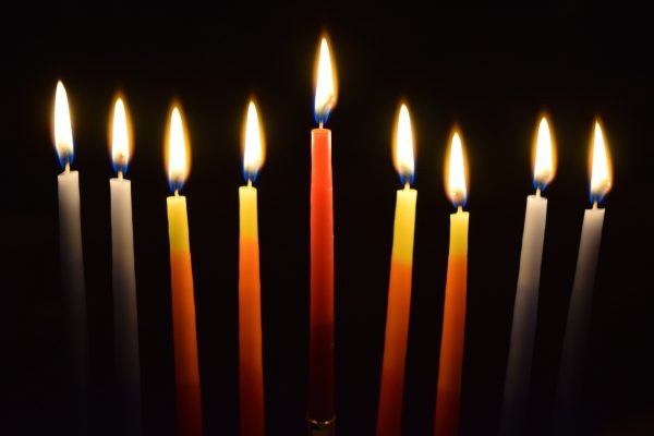 Nine lit candles of various colors burning in the dark, arranged in a straight line.