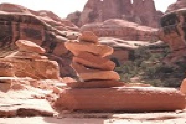 Stacked rocks in a desert landscape with red rock formations in the background.
