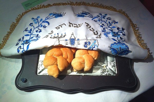 two braided challah under a white and blue cover
