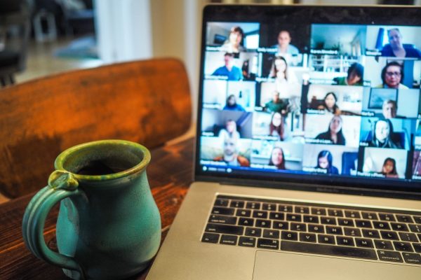 A laptop displaying a virtual meeting with multiple participants, next to a green mug on a wooden table.