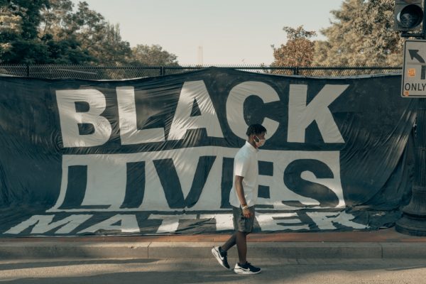 Person walking past a large Black Lives Matter banner on a sunny day.