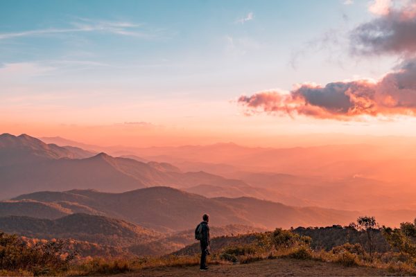 landscape of pink-tinted mountains with person standing and sky above with one cloud on the right side