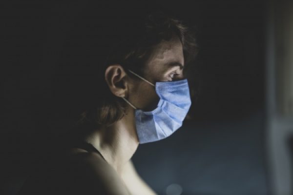 Person wearing a blue face mask, looking to the side in dim lighting.