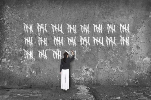 A woman draws tally marks in chalk on a textured concrete wall.