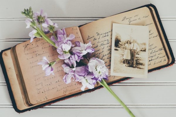 Open journal with handwritten text, a purple floral stem, and a vintage black-and-white photo on a white surface.