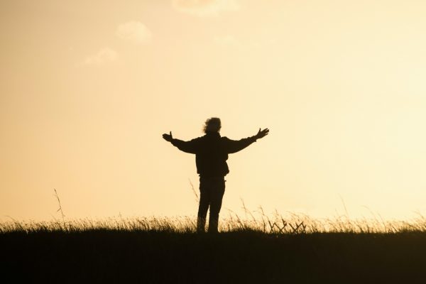 Silhouette of a person standing with arms outstretched against a golden sky at sunset.