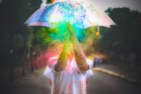 person holding white umbrella with multi-colored paint or sparkles raining down over them