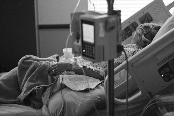 Person resting in a hospital bed, with an IV drip attached and medical equipment nearby.