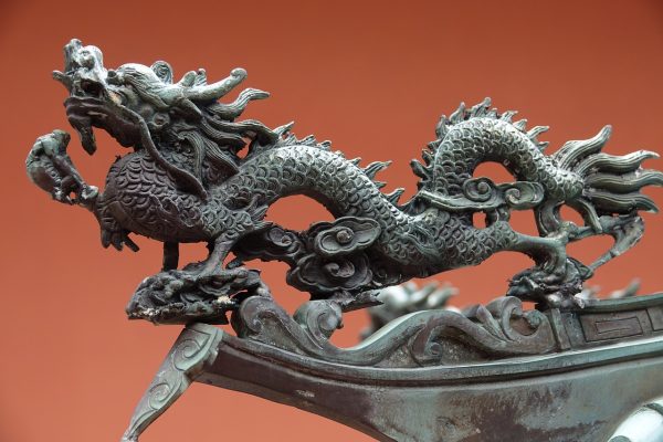 Bronze sculpture of a dragon with detailed scales and claws, set against a reddish background.