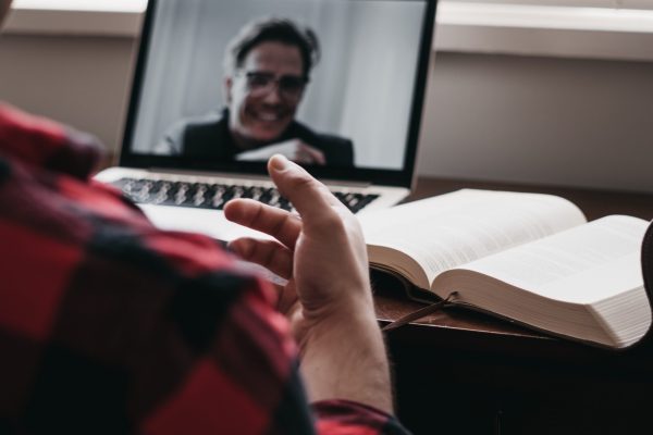 person having online call or meeting with someone on the computer. live person is shown with hand as if gesturing in conversation. person on computer is smiling.