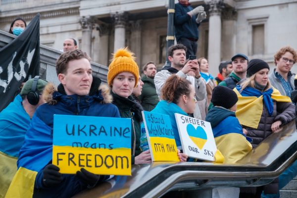 People at a protest holding signs in support of Ukraine with a historic building in the background.